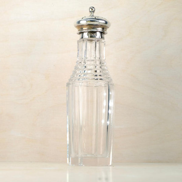Clear glass bottle with silver lid on a beige background