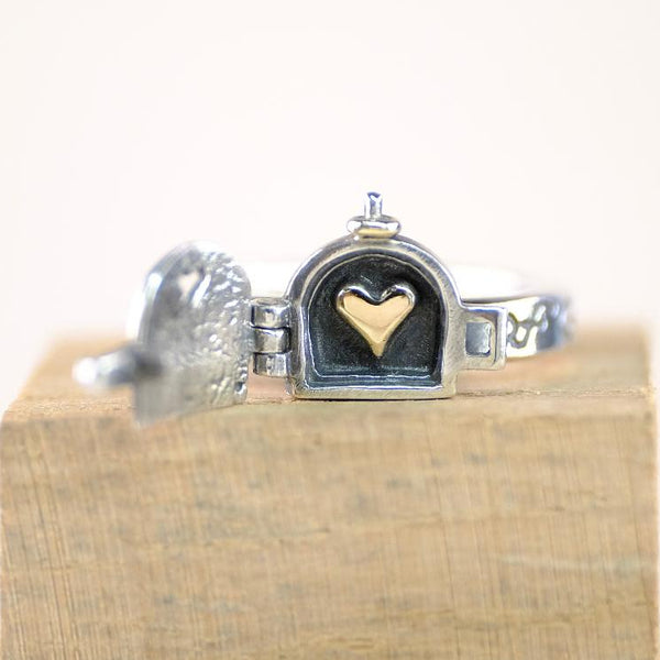 Silver ring with a heart charm on a wooden block against a white background
