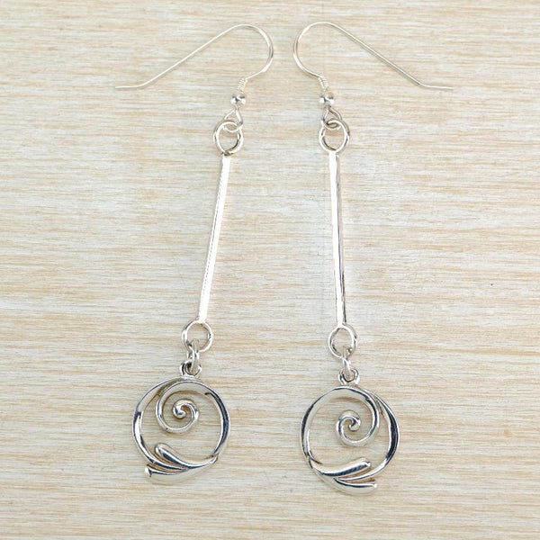 A pair of silver dangle earrings with spiral drop charms, displayed on a light wood grain background.