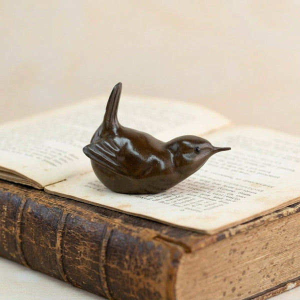 A small dark bronze bird figurine, resembling a wren, displayed on a book