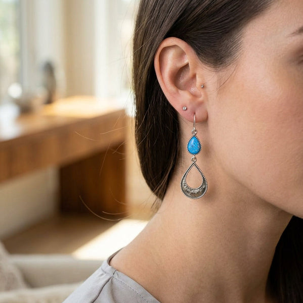 A pair of silver dangle earrings with teardrop-shaped light blue opal gemstones and textured silver teardrop charms.