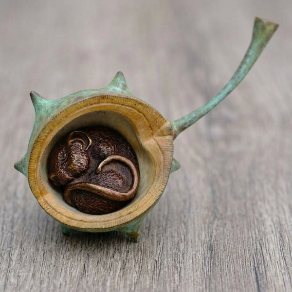 A small decorative object with a spiky greenish-brown conker shell made from bronze shown open to reveal a curled bronze mouse 