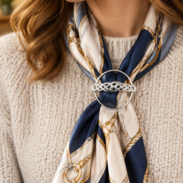 A silver ring with a flat circular band and a domed central Celtic knot design, displayed on a scarf
