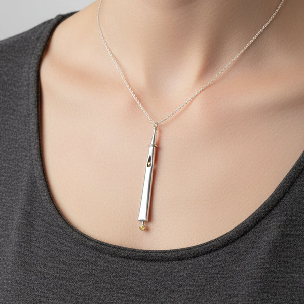 A long silver pendant necklace embellished with a gold heart and a citrine displayed on top of a gray box on a light wood background.