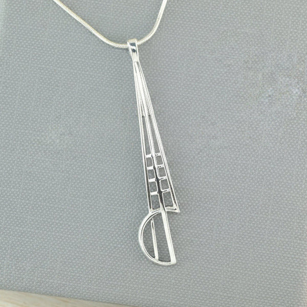 A silver pendant necklace with a geometric, openwork design resting on a textured gray Smithsonia gift box. The necklace chain is visible at the top.