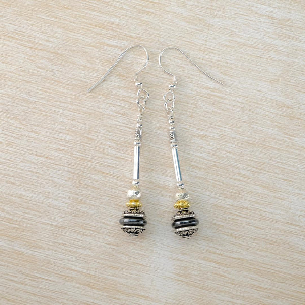 Pair of silver earrings with black and gold beads on a light wood surface