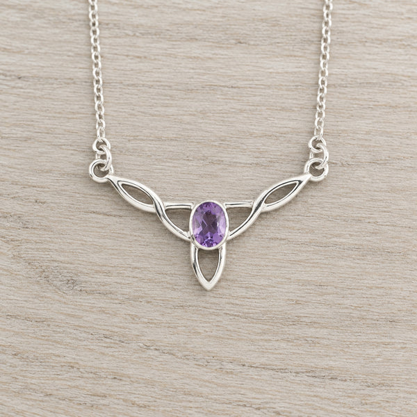 A silver Celtic knot pendant necklace with an oval purple amethyst centre stone, displayed on a gray background.