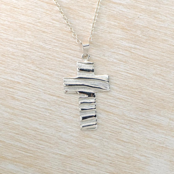 Silver cross pendant on a chain against a light wood background