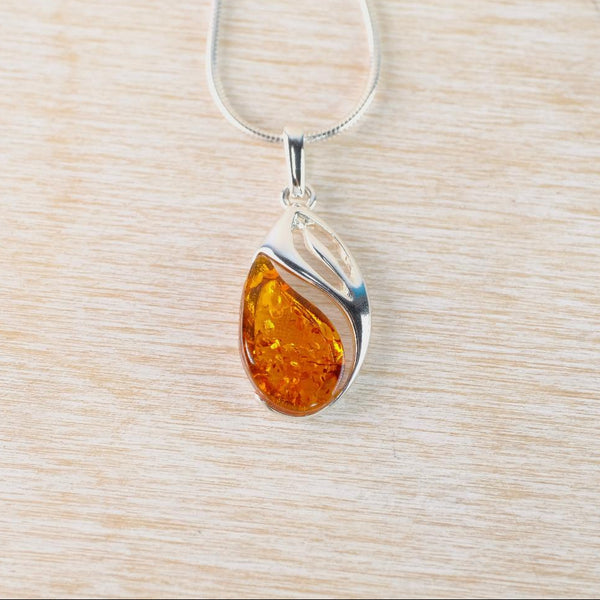 Teardrop-shaped amber pendant on a silver chain against a light wood background