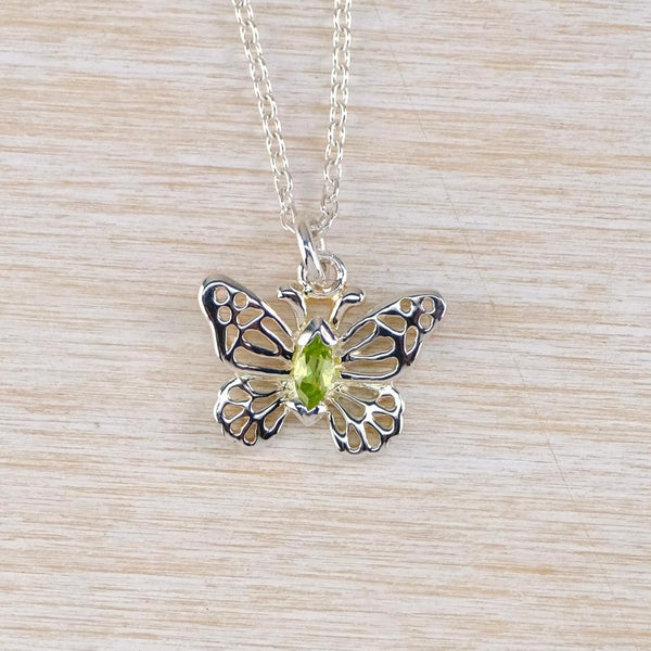 Silver butterfly pendant with a green gemstone on a wooden surface