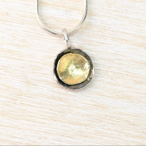 Necklace with a gold and silver pendant on a light wood surface