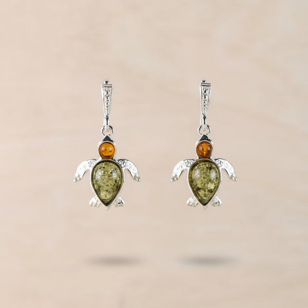 Turtle-shaped earrings with green and orange  amber stones against a beige background