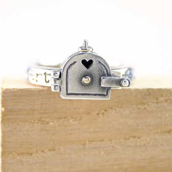 Silver ring with a heart design on a wooden block against a white background