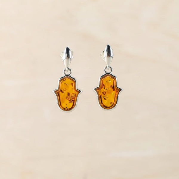 Amber hamsa hand earrings against a beige background