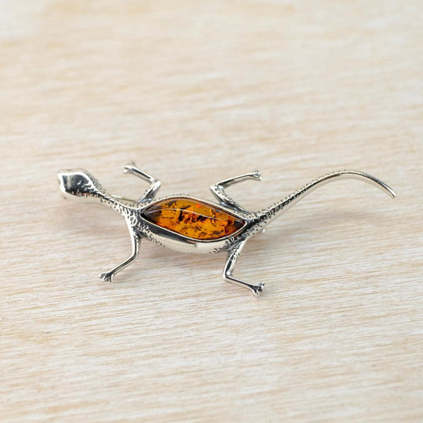 Silver lizard-shaped brooch with amber center on a light wood background