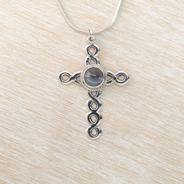 Silver cross pendant with a central gemstone on a light wood surface