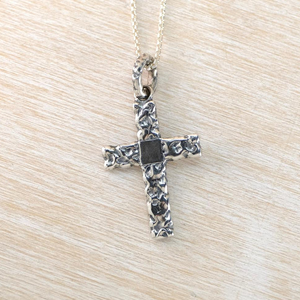 Silver cross pendant on a chain against a beige background