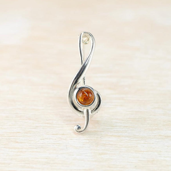 Silver treble clef  brooch with a central amber stone on a light wood background