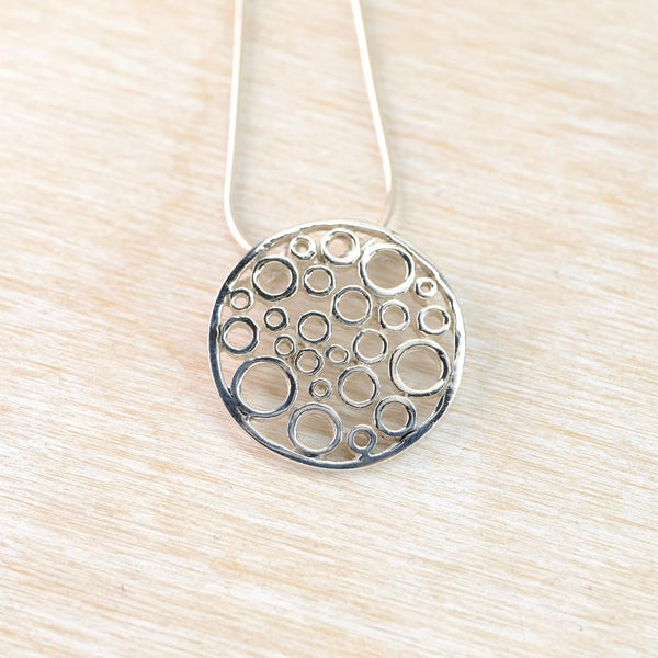 Silver circular pendant with bubble design on a light wood surface