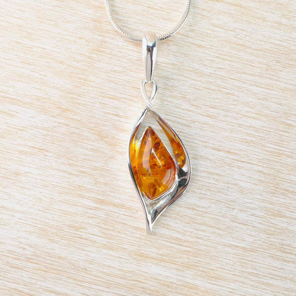 Teardrop-shaped amber pendant on a silver chain against a light wood background
