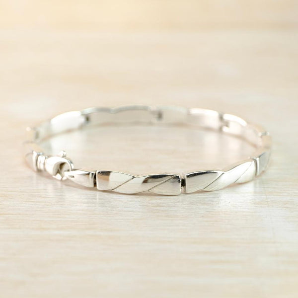 Silver linked bracelet with a simplified twist design on a light beige background