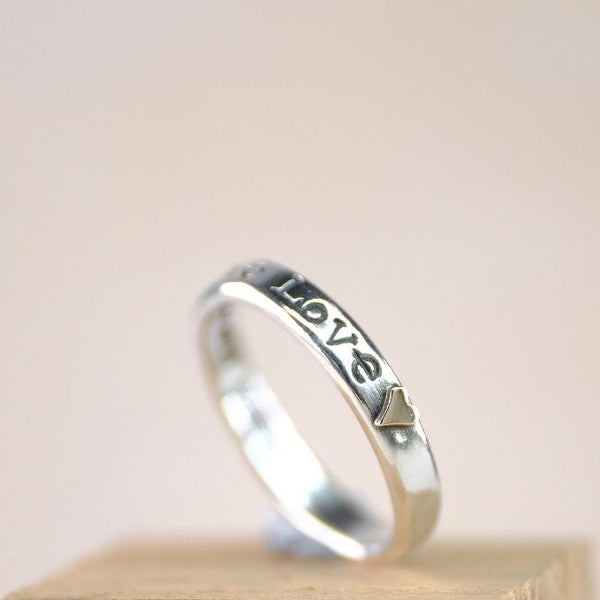 Silver ring with 'LOVE' engraving on a wooden block against a beige background