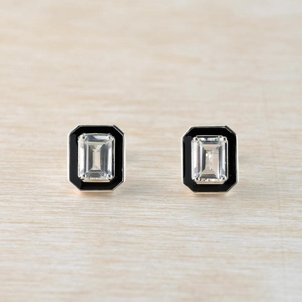 Pair of emerald-cut clear gemstone earrings with black enamel on a beige background