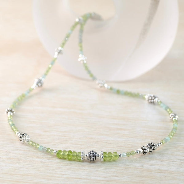 Beaded necklace with green and silver beads on a light wooden surface