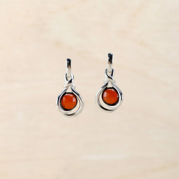 Pair of silver earrings with amber gemstones on a beige background