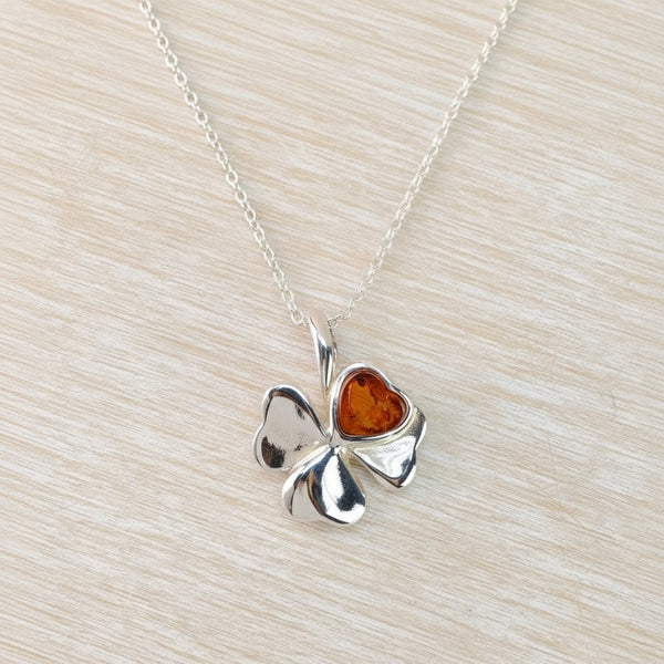 Silver four-leaf clover pendant with amber center on a light wood surface
