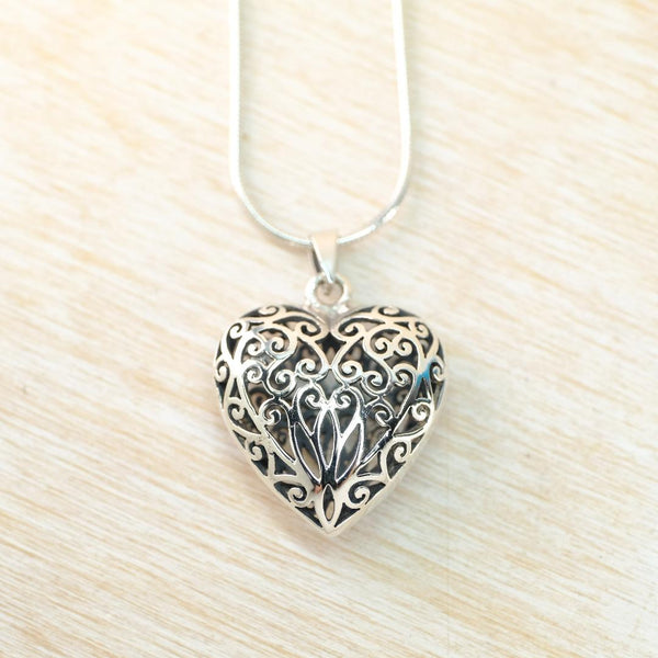 Silver heart-shaped pendant with intricate designs on a light wood background