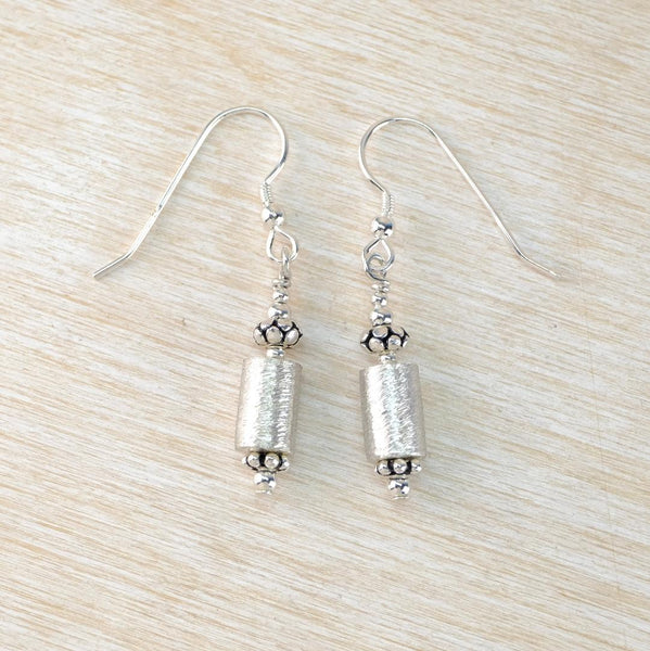 Silver cylindrical earrings on a light wood surface