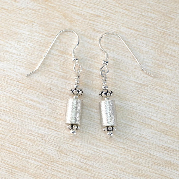 Silver cylindrical earrings on a light wood surface