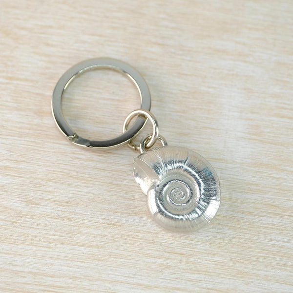 Keychain with a silver spiral shell charm on a light wood surface