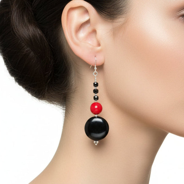 Pair of earrings with black and red beads on a beige background