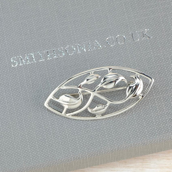 A silver brooch with an openwork floral design, displayed on a textured gray Smithsonia box.