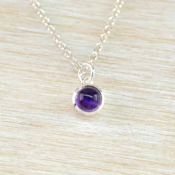 A small round silver and lilac stoned pendant hanging from a oval linked silver chain. The pale lilac smooth stone is set in a shiny round frame with a shiny silver ring for the chain to thread through.