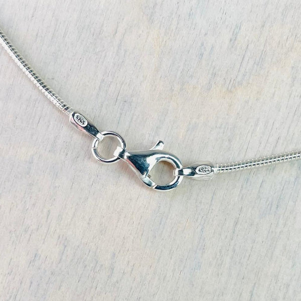 Close-up of a silver necklace clasp on a light wooden surface