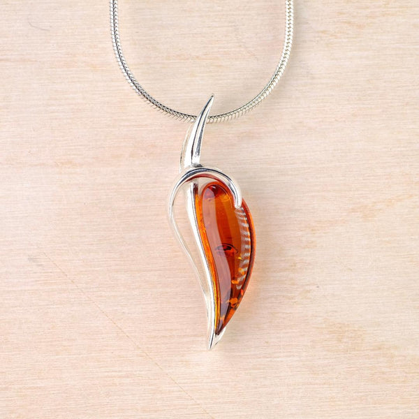Silver pendant set with deep orange coloured amber on a light wood background