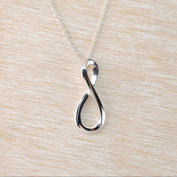 Silver infinity pendant necklace on a light wood surface