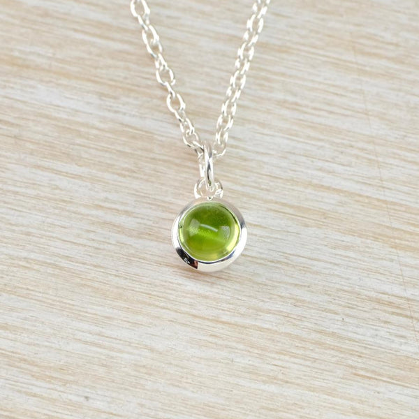 A small round silver and green stoned pendant hanging from a oval linked silver chain. The pale lime green smooth stone is set in a shiny round frame with a shiny silver ring for the chain to thread through.