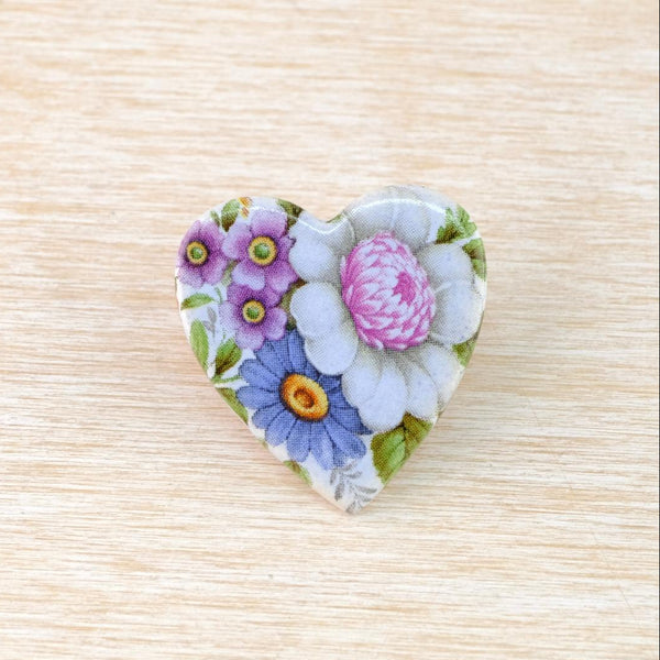 a flat heart-shaped ceramic brooch transfer printed on its front side with a vintage inspired pattern of pretty little flowers in light blues, violets and pinks