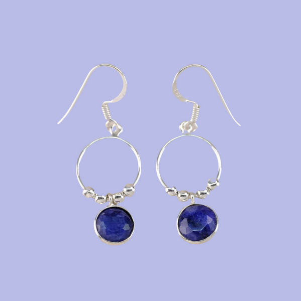 Pair of silver hoop earrings with blue gemstones on a wooden surface