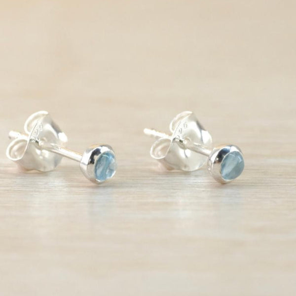 A pair of silver and blue stoned stud earrings. A round smooth pale blue stone sits proud of a polished silver surround with a buttertly fitting on a silver post attached centrally.