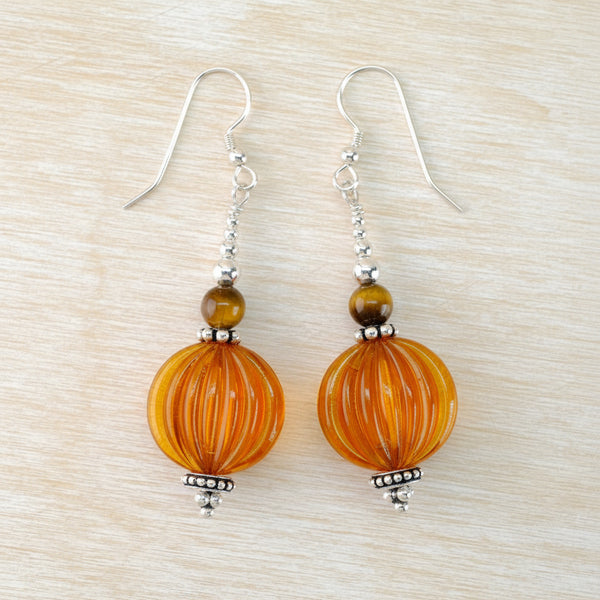 Pair of orange beaded earrings on a beige background