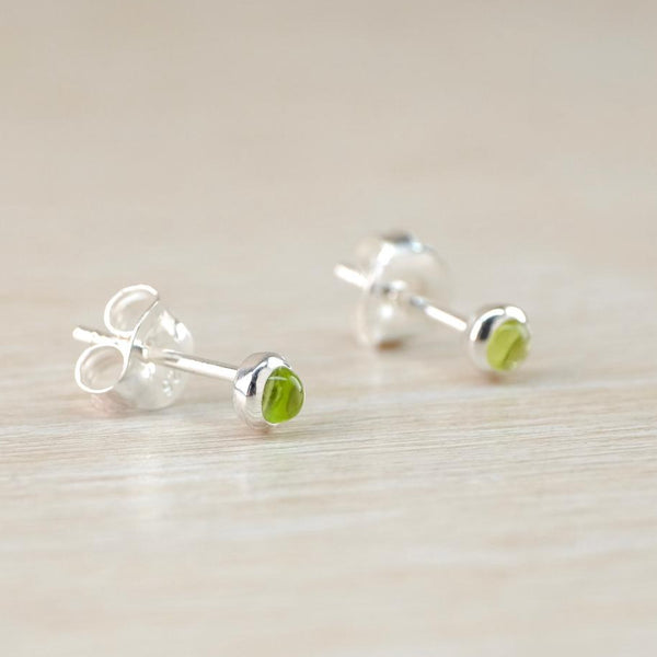 A pair of silver and green stoned stud earrings. A round smooth pale lime green stone sits proud of a polished silver surround with a buttertly fitting on a silver post attached centrally.