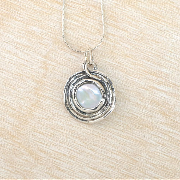 Silver necklace with a circular pendant featuring a pearl on a beige background