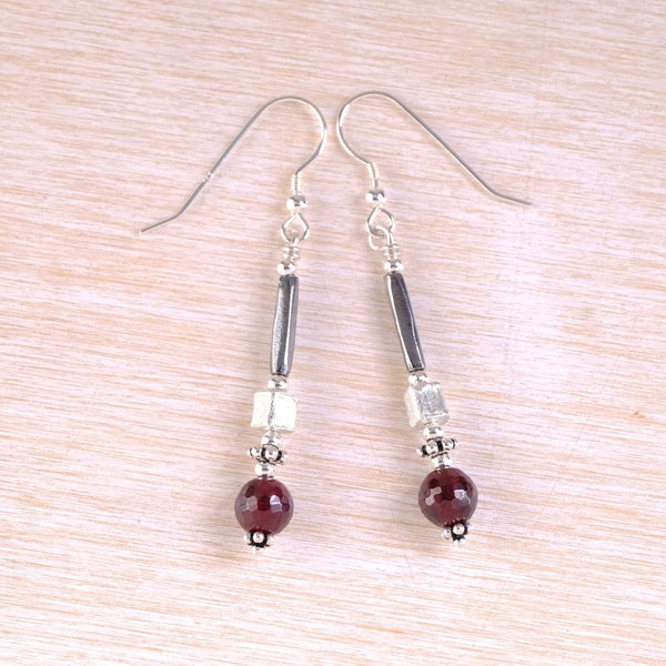 Pair of silver earrings with red beads on a light wood surface