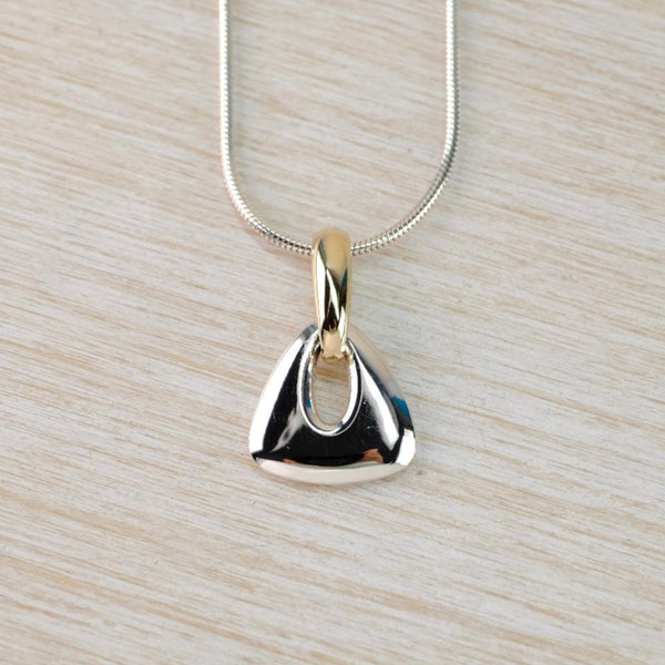 Gold and silver pendant on a chain. A soft triangle in silver has an oval hole through which the gold bale is attached. the silver chain is threaded through the gold bale.