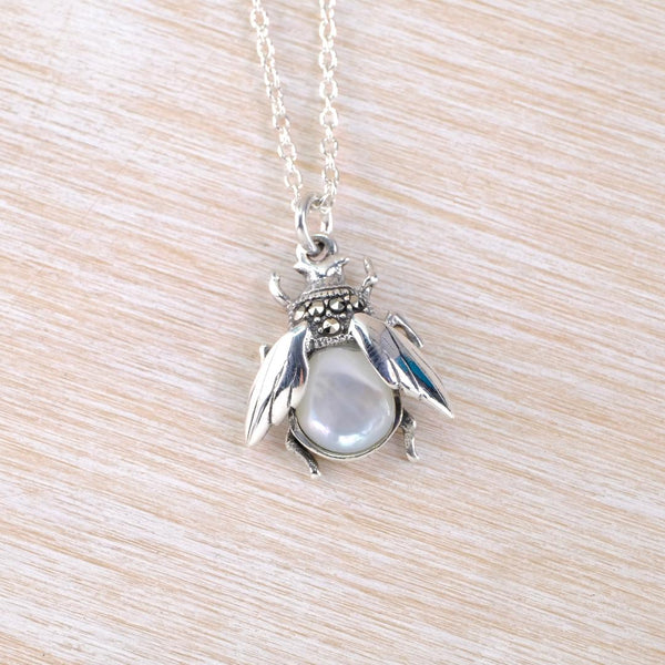 Silver bee pendant with a mother of pearl body on a chain against a light wood background